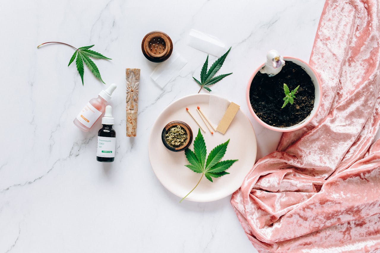 Home 1 Flat lay of cannabis leaves, CBD oils, and accessories on marble surface.